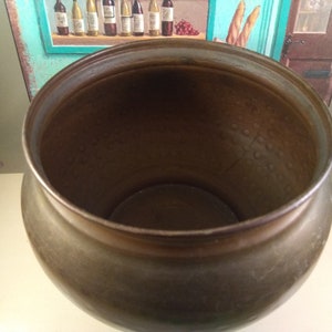 May include: A large, round, copper pot with a hammered finish. The pot is empty and has a shiny, metallic surface.
