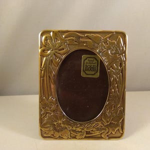 Puede incluir: Un marco de fotos dorado con un diseño floral ornamentado. El marco tiene una pequeña etiqueta que dice "Hand polished SOLID BRASS".