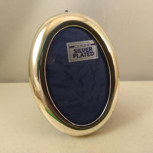 Peut inclure: Un cadre photo ovale en argent plaqué avec un fond en velours bleu. Le cadre porte une étiquette indiquant "Argent véritable plaqué".