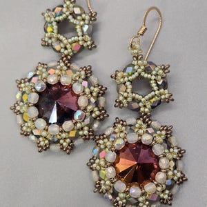 Pode incluir: Brincos pendurados com uma parte superior em forma de estrela e uma grande pedra central redonda e facetada em tons de roxo e laranja. Os brincos são adornados com contas iridescentes e acessórios de metal dourado. Joias feitas à mão.