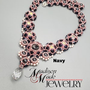 May include: A beaded necklace with a teardrop crystal pendant. The necklace is made with black, pink, and gray beads. The necklace is labeled "Navy".
