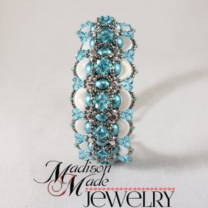 May include: A turquoise and white beaded bracelet with a geometric design. The bracelet is made with small round beads and faceted crystals.