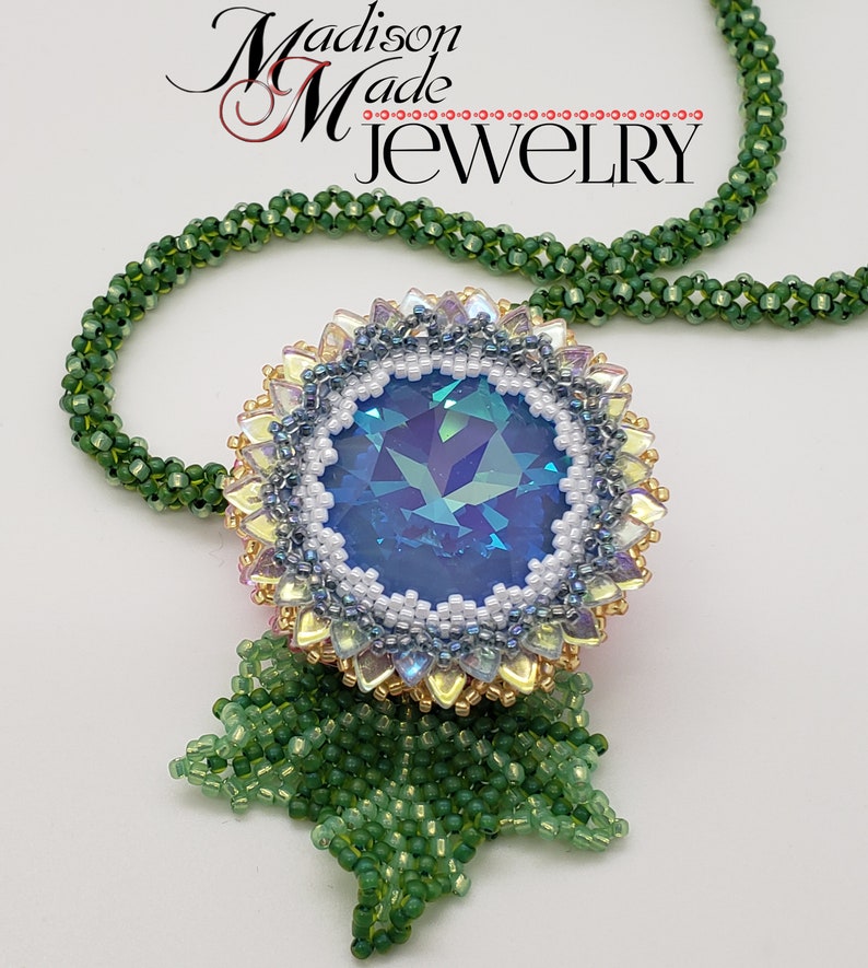 May include: A beaded necklace with a large blue iridescent crystal surrounded by white, gold, and pink beads. The pendant is attached to a green beaded chain. The necklace is labeled "Madison Made Jewelry".