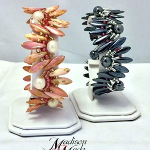 May include: Two bracelets made with beads. One bracelet is made with pink and white beads and the other is made with black and red beads. Both bracelets are on white display stands. The text "Madison Made Jewelry" is at the bottom of the image.