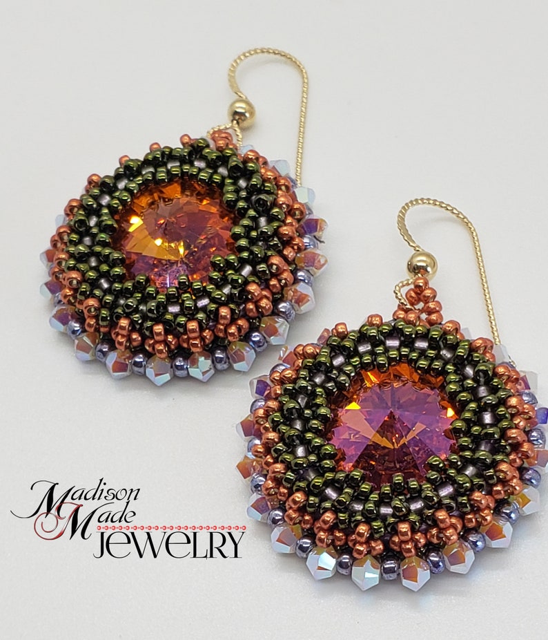 Puede incluir: Un par de pendientes de cuentas con un dise&ntilde;o redondo multicolor. Los pendientes presentan un gran cristal naranja facetado en el centro de cada pendiente. Los pendientes est&aacute;n hechos con cuentas de cobre, verdes y moradas.