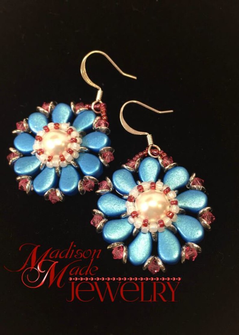 May include: A pair of blue and silver flower-shaped earrings with a white pearl in the center. The earrings are made with small beads and have a silver hook closure. The earrings are on a black background with the text "Madison Made Jewelry" in red.