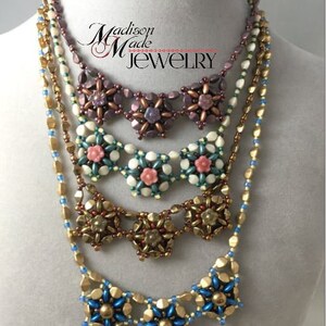 May include: A layered necklace with five strands of beads. The top strand is a dark purple with a flower design. The second strand is a cream color with a flower design. The third strand is a gold color with a flower design. The fourth strand is a light blue with a flower design. The bottom strand is a gold chain. The necklace is on a white mannequin.