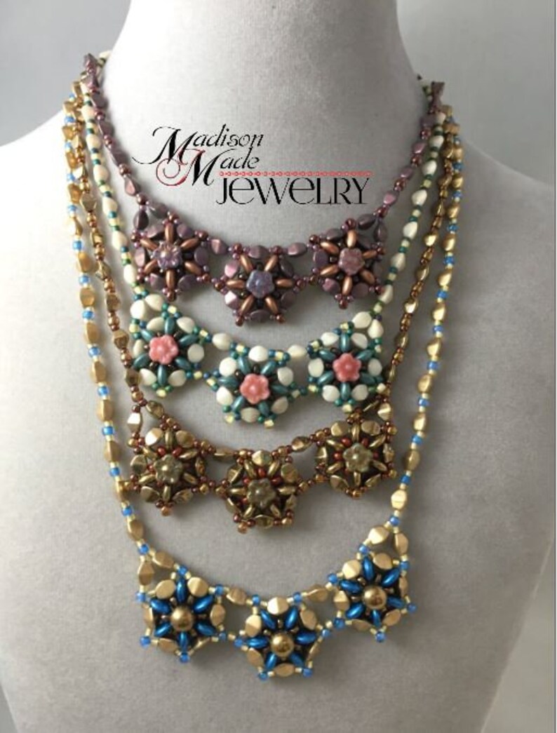 May include: A layered necklace with five strands of beads. The top strand is a dark purple with a flower design. The second strand is a cream color with a flower design. The third strand is a gold color with a flower design. The fourth strand is a light blue with a flower design. The bottom strand is a gold chain. The necklace is on a white mannequin.