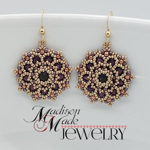 May include: A pair of handmade beaded earrings. Each earring features a gold-colored hook and a circular design with a dark purple center and a gold and copper-colored beaded pattern. The earrings are set against a white background. The text "Madison Made Jewelry" is visible.