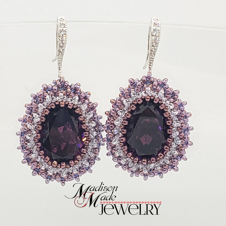 May include: A pair of dangle earrings with a large, faceted, dark purple gemstone surrounded by a beaded halo of silver, white, and purple beads.