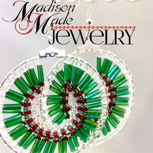 May include: A pair of green and red beaded earrings with a spiral design. The earrings are made with small, round beads and are attached to silver hooks.