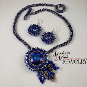May include: A blue and silver beaded necklace with a large blue crystal pendant and matching earrings. The necklace is made with a delicate chain and the pendant is a large, round crystal with a silver setting. The earrings are small and round with a silver setting and a blue crystal.