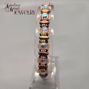 May include: A beaded bracelet with iridescent, gold, and brown beads. The bracelet is on a clear display stand.