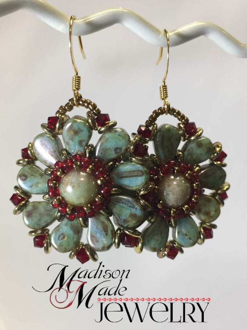 May include: A pair of gold earrings with a floral design. The flowers are made of turquoise and white beads with red accents. The earrings are hanging from gold hooks.
