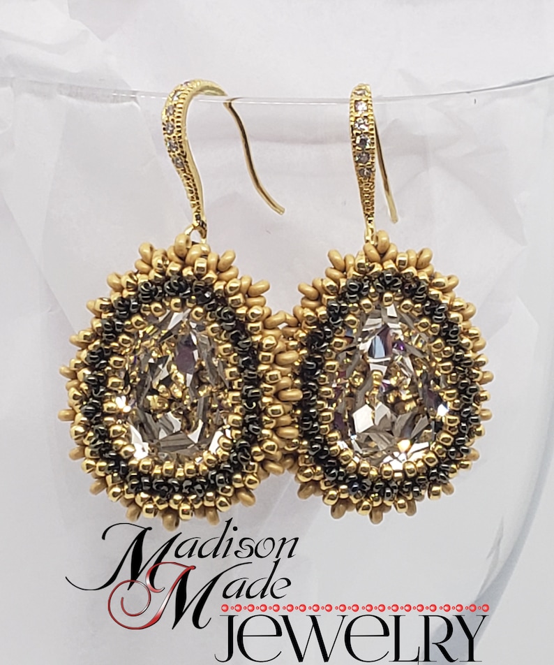 May include: Gold tone earrings with a teardrop-shaped crystal center surrounded by black and gold beads. The earrings have a hook closure.