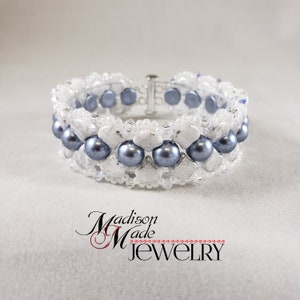 Op de afbeelding: Een witte en grijze kralen armband met een zilveren sluiting. De armband heeft een rij grijze parels en een rij witte kralen.
