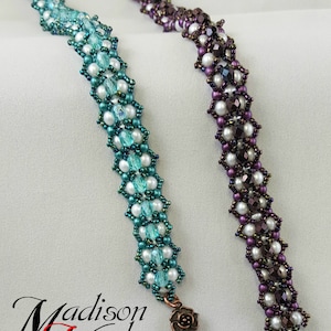 May include: Two beaded bracelets with a floral design. The bracelet on the left is teal and white, and the bracelet on the right is purple and white. Both bracelets have a copper-colored clasp with a floral design.