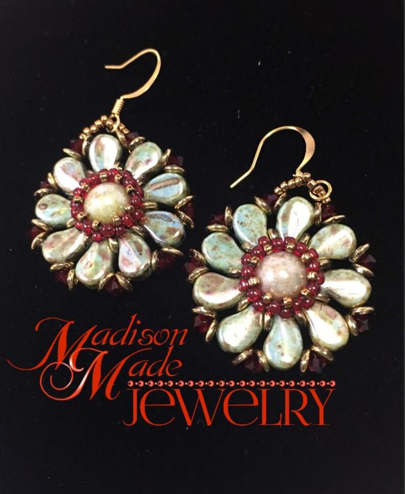 May include: A pair of gold tone earrings with a flower design. The flowers are made of iridescent green and white beads with red beads in the center. The earrings are hanging from gold hooks.
