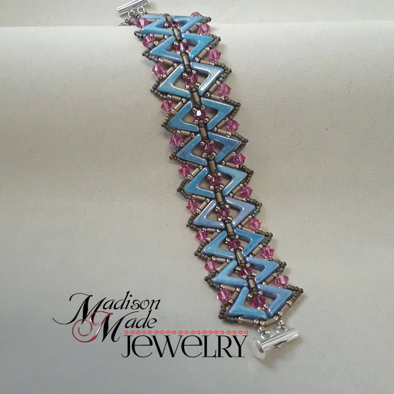 May include: A blue and pink beaded bracelet with a silver clasp. The bracelet is made with small, triangular beads and features a chevron pattern.