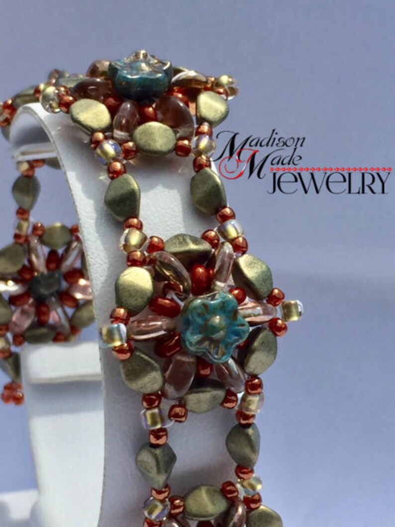 May include: A beaded bracelet with a multi-colored design featuring brown, gold, red, and blue beads. The bracelet is made with a variety of different sized beads and has a unique, intricate design. The bracelet is on a white display stand.  Madison Made Jewelry.