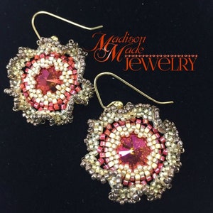May include: A pair of gold earrings with a red and white beaded flower design. The center of each flower has a red crystal. The earrings are labeled "Madison Made Jewelry".