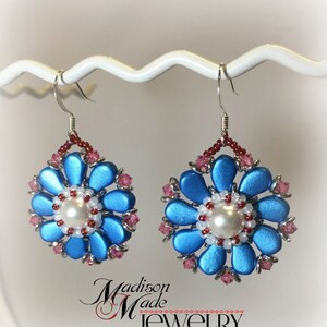 May include: A pair of blue and pink flower-shaped earrings with a pearl in the center. The earrings are made with beads and have a silver hook.