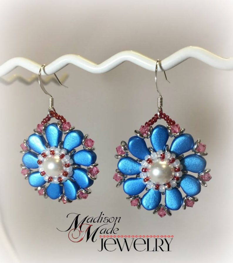 May include: A pair of blue and pink flower-shaped earrings with a pearl in the center. The earrings are made with beads and have a silver hook.