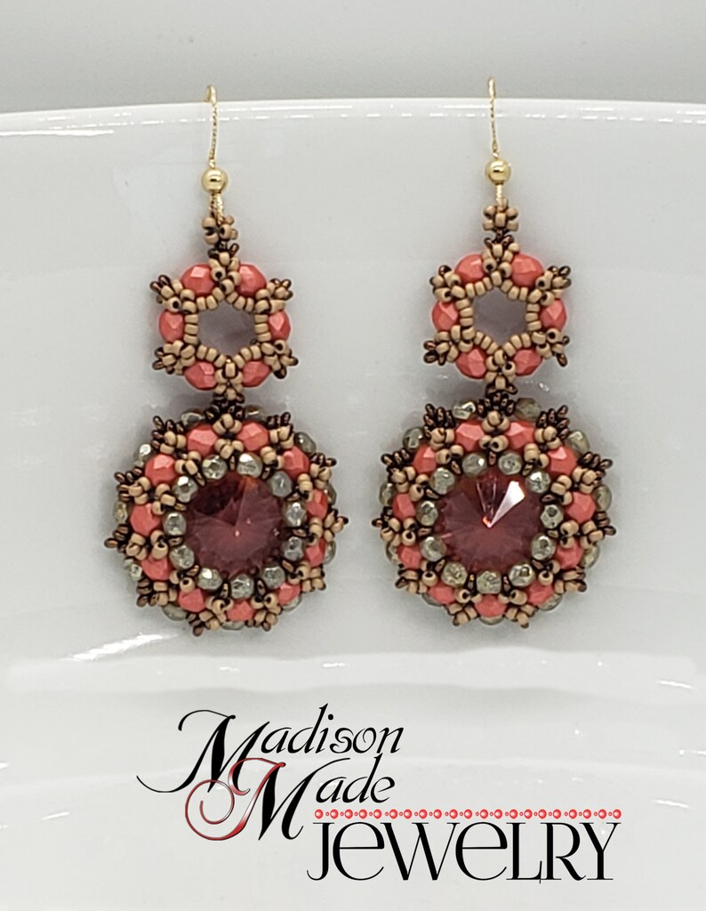 May include: A pair of dangle earrings with a peach and brown color scheme. The earrings feature a round bead with a crystal center and a smaller hexagonal bead above it.