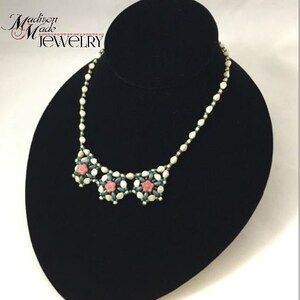 May include: A white and green beaded necklace with pink flower accents. The necklace is displayed on a black velvet bust form. The text "Madison Made Jewelry" is visible in the top left corner of the image.