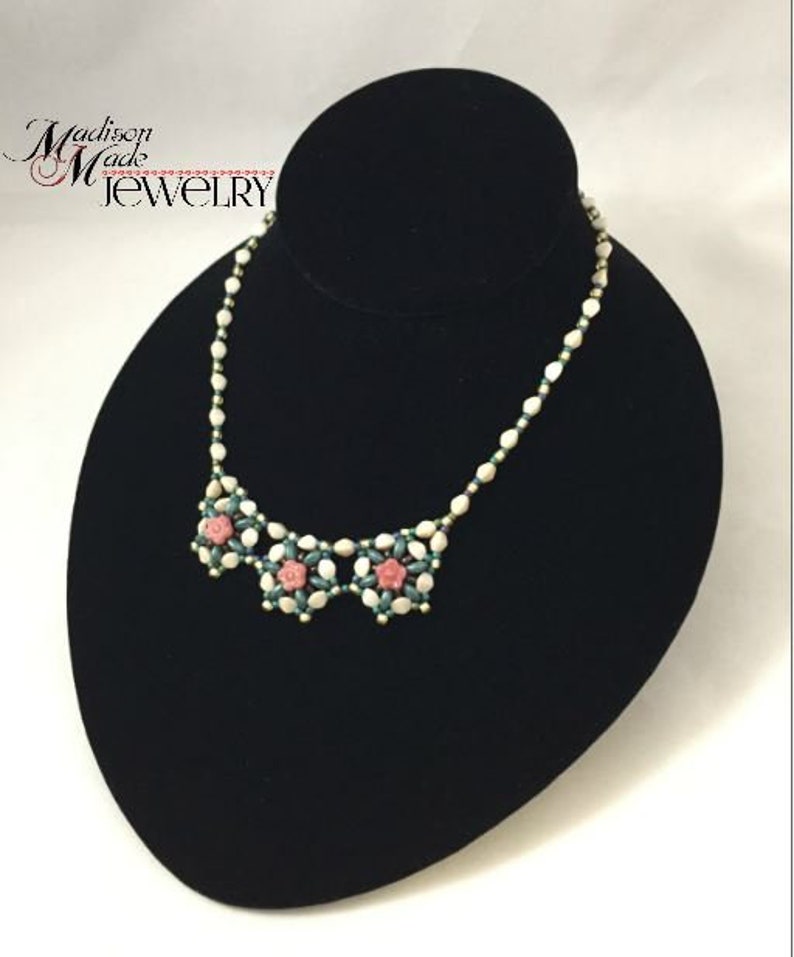 May include: A white and green beaded necklace with pink flower accents. The necklace is displayed on a black velvet bust form. The text "Madison Made Jewelry" is visible in the top left corner of the image.