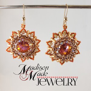May include: A pair of gold earrings with a starburst design. The earrings are made with small beads in shades of gold, orange, and clear. The centre of each earring features a large, iridescent, orange crystal.