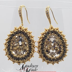 May include: A pair of gold dangle earrings with a clear crystal teardrop stone surrounded by gold and black beads. The earrings have a gold hook closure.