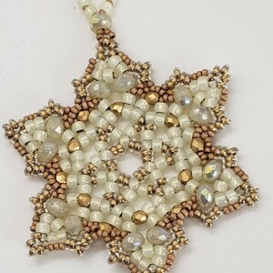 May include: A white and gold beaded snowflake ornament with a loop for hanging.