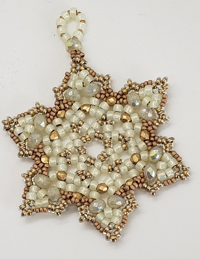 May include: A white and gold beaded snowflake ornament with a loop for hanging.