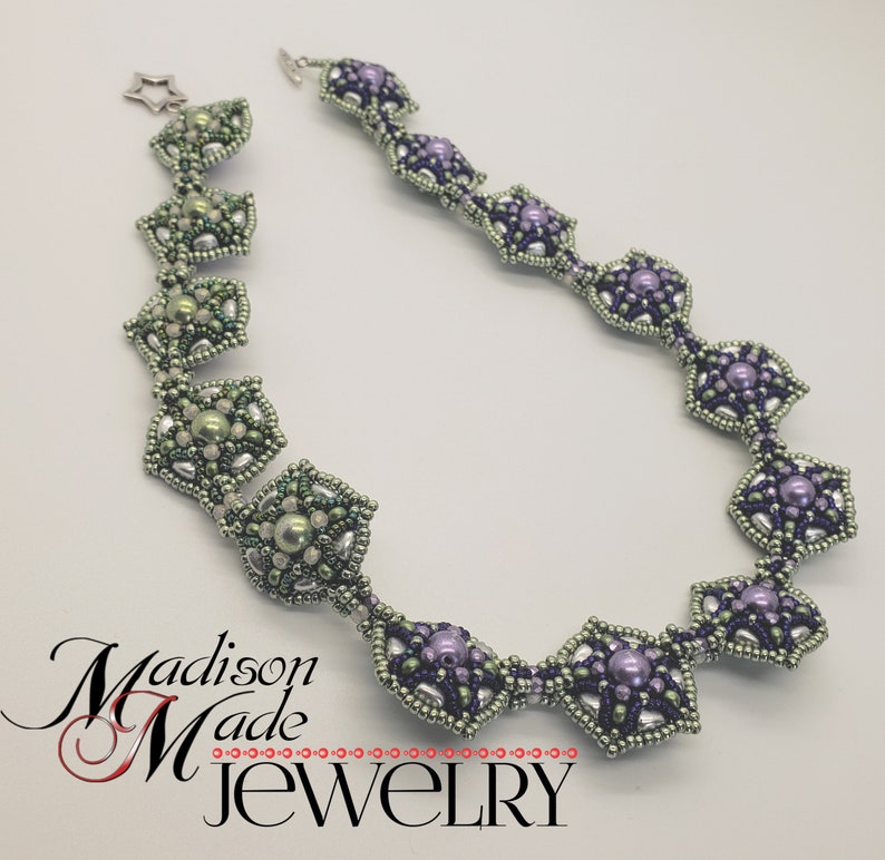 May include: A delicate necklace made with silver and green and purple beads, arranged in a geometric pattern. The necklace is made by Madison Made Jewelry.