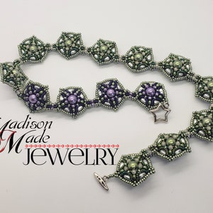 May include: A silver beaded necklace with green and purple beads arranged in a starburst pattern. The necklace has a star-shaped clasp and the text "Madison Made Jewelry" is visible in the lower left corner of the image.