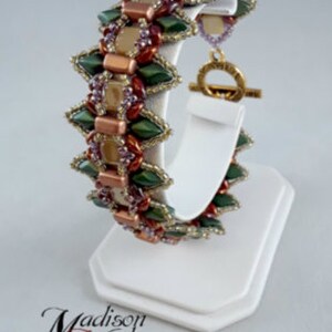 May include: A beaded bracelet with a geometric design. The bracelet features green, copper, and purple beads. It is displayed on a white stand. The bracelet has a gold-colored clasp. The text "Madison Made Jewelry" is at the bottom.