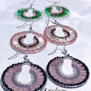 May include: A set of four pairs of beaded earrings. The earrings are made with small, colorful beads and are available in pink, green, and purple. The earrings are all circular in shape and have a silver hook closure.