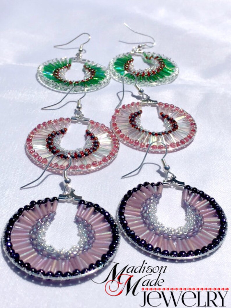 May include: A set of four pairs of beaded earrings. The earrings are made with small, colorful beads and are available in pink, green, and purple. The earrings are all circular in shape and have a silver hook closure.