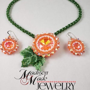 May include: A green beaded necklace with a peach and white flower pendant and matching earrings. The pendant features a large iridescent crystal in the center. The necklace and earrings are labeled "Madison Made Jewelry".