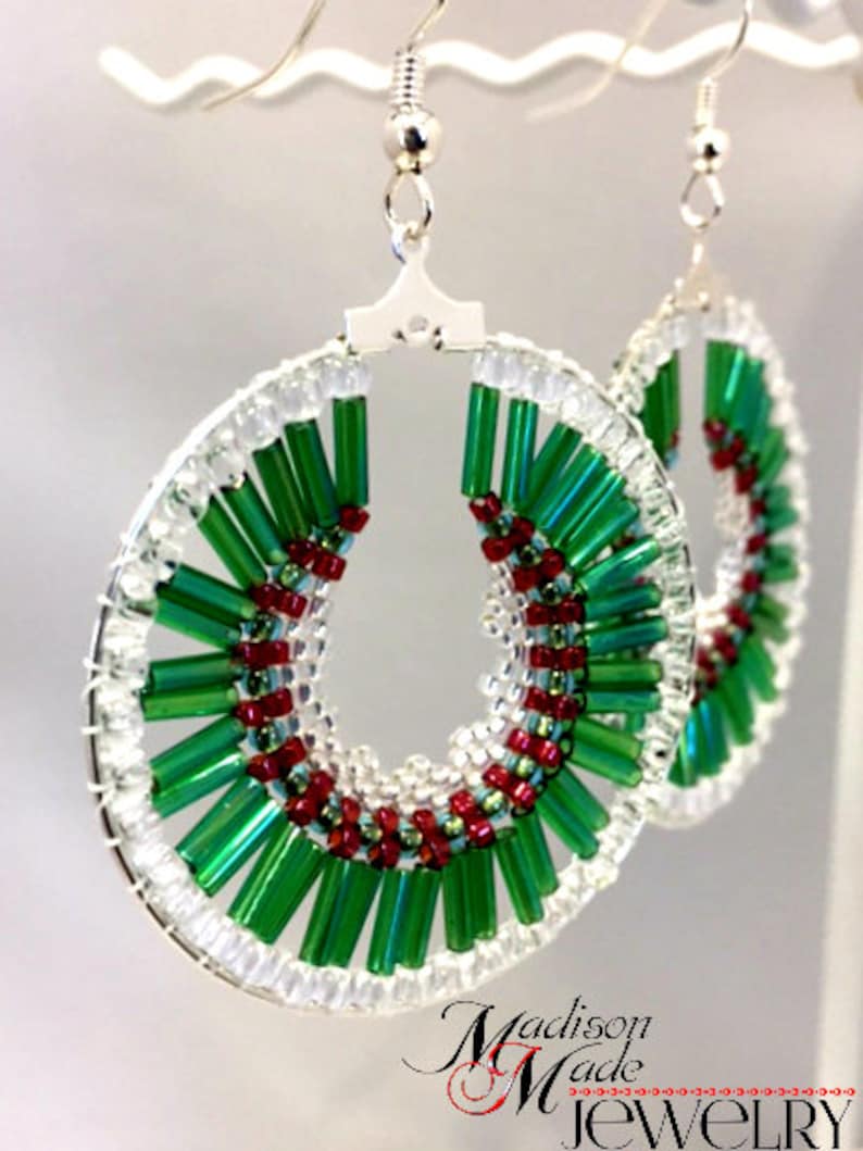 May include: A pair of green and red beaded hoop earrings with silver hooks. The beads are arranged in a spiral pattern.
