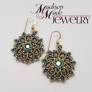 May include: A pair of handmade beaded earrings. The earrings feature a circular design with a central iridescent gem, surrounded by copper, green, and blue beads. The earrings have gold-colored ear wires. The text "Madison Made Jewelry" is in the upper right corner.