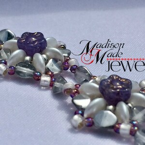 May include: A close-up of a beaded bracelet with white and purple beads. The bracelet features a flower design with a purple center. The text "Madison Made Jewelry" is visible in the background.