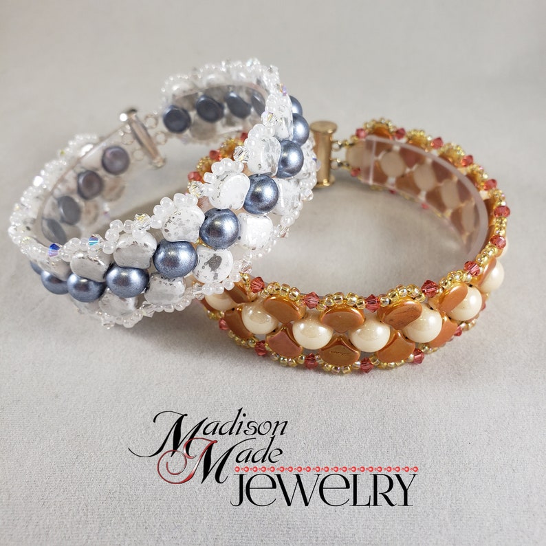 Op de afbeelding: Twee kralenarmbanden, een met witte en grijze kralen en de andere met bruine en cr&egrave;mekleurige kralen. De armbanden liggen op elkaar.