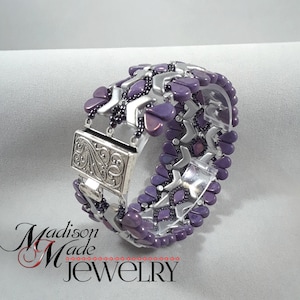 May include: A purple and silver beaded bracelet with a silver clasp. The bracelet is made with a geometric pattern and has a silver clasp with a floral design.