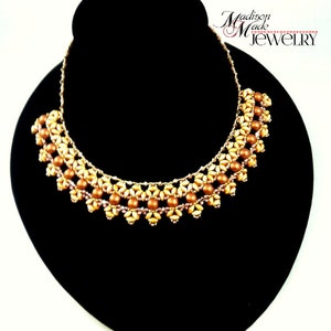 May include: A gold and brown beaded necklace with a delicate floral design. The necklace is displayed on a black jewelry stand. The text "Madison Made Jewelry" is visible in the top right corner of the image.