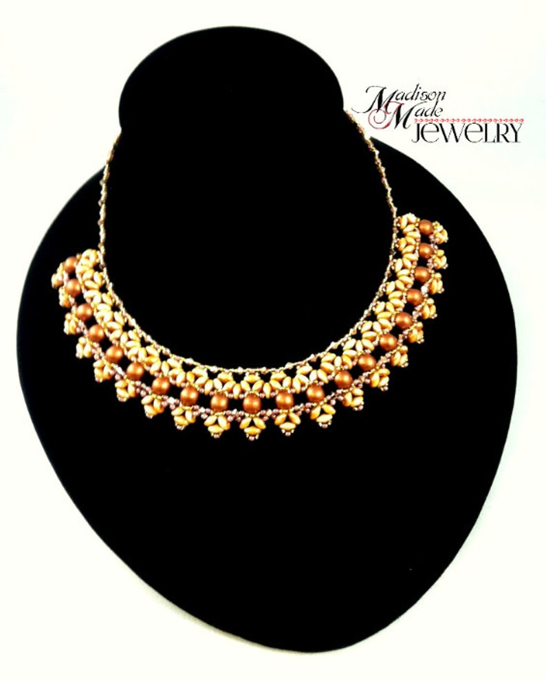 May include: A gold and brown beaded necklace with a delicate floral design. The necklace is displayed on a black jewelry stand. The text "Madison Made Jewelry" is visible in the top right corner of the image.