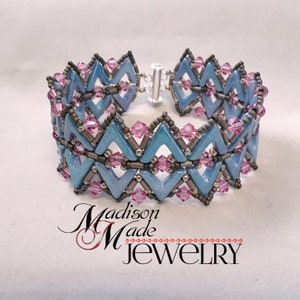 May include: A blue and silver beaded bracelet with pink accents. The bracelet is made with a chevron pattern and has a silver clasp.