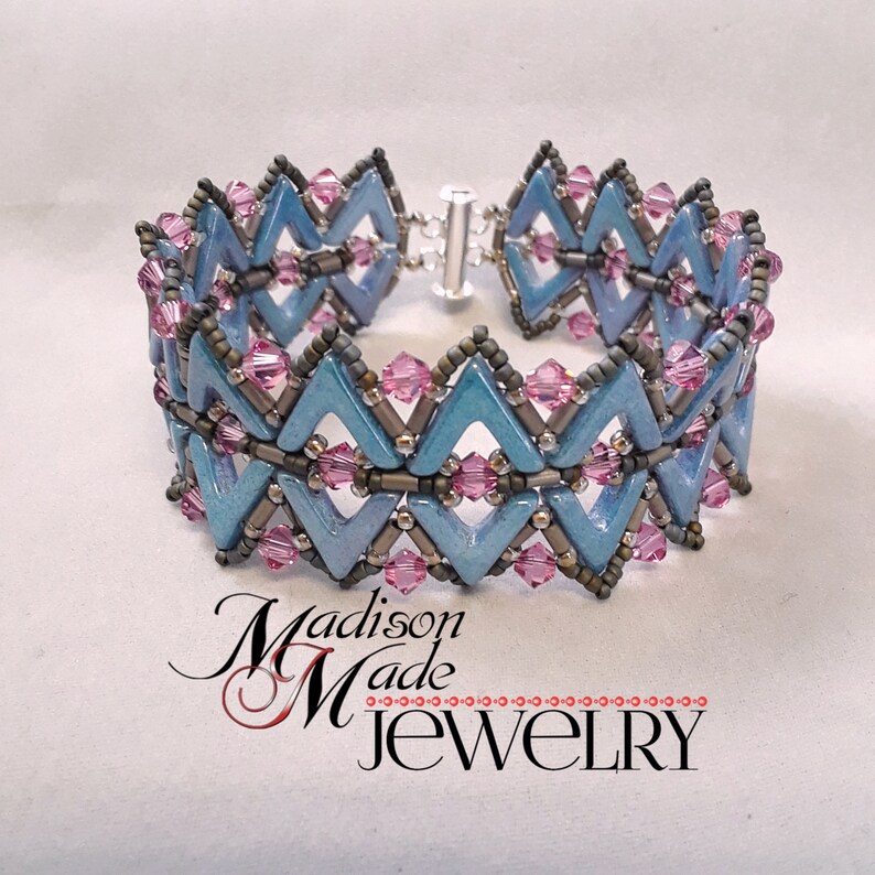 May include: A blue and silver beaded bracelet with pink accents. The bracelet is made with a chevron pattern and has a silver clasp.