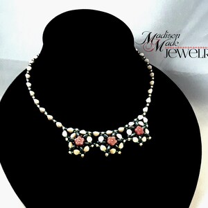 May include: A white and green beaded necklace with pink flower accents. The necklace is displayed on a black jewelry stand. The text "Madison Made JEWELRY" is visible in the upper right corner of the image.